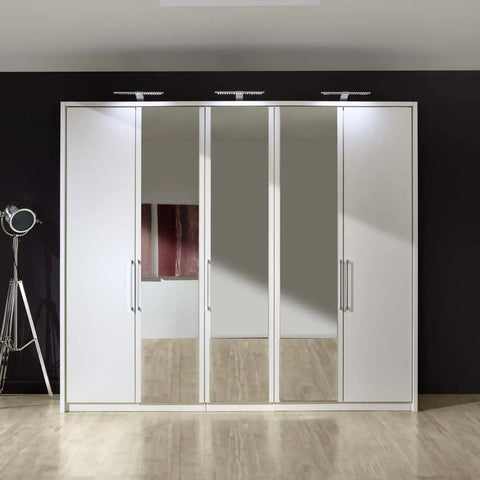 Image of Wiemann Bristol White 5 Door Wardrobe with Mirror. Option of Matt or Glass finish on side doors, with middle doors featuring mirror pads. Dimensions: Width 250cm, Height 216cm, Depth 58cm. Free Delivery and Assembly. 12 months interest-free pay monthly available. - Front View Lifestyle Image