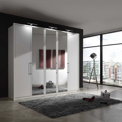 Image of Wiemann Bristol White 5 Door Wardrobe with Mirror. Option of Matt or Glass finish on side doors, with middle doors featuring mirror pads. Dimensions: Width 250cm, Height 216cm, Depth 58cm. Free Delivery and Assembly. 12 months interest-free pay monthly available. - Side View Lifestyle Image